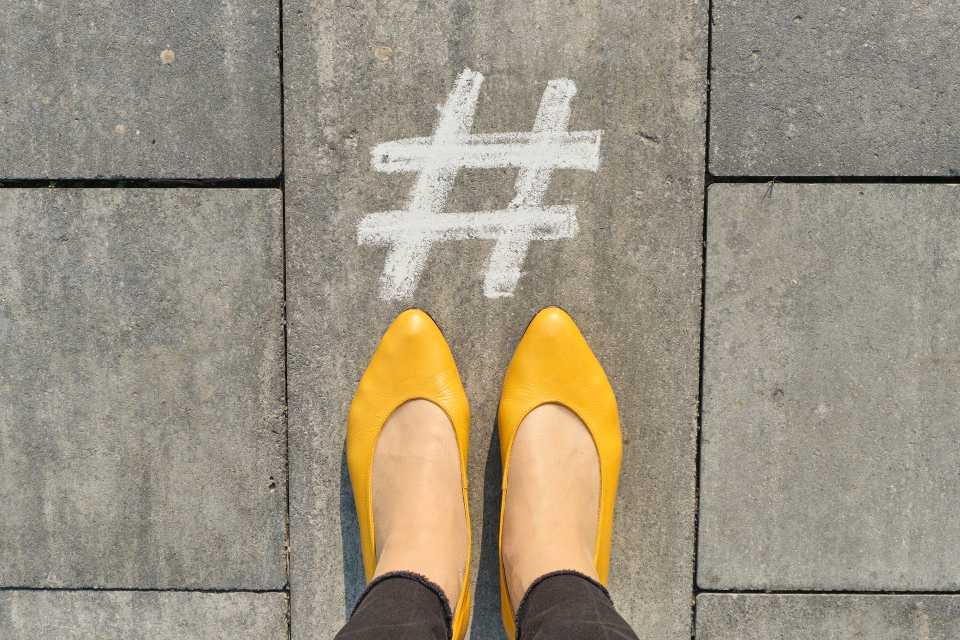 hashtag symbol on gray sidewalk with woman legs top view